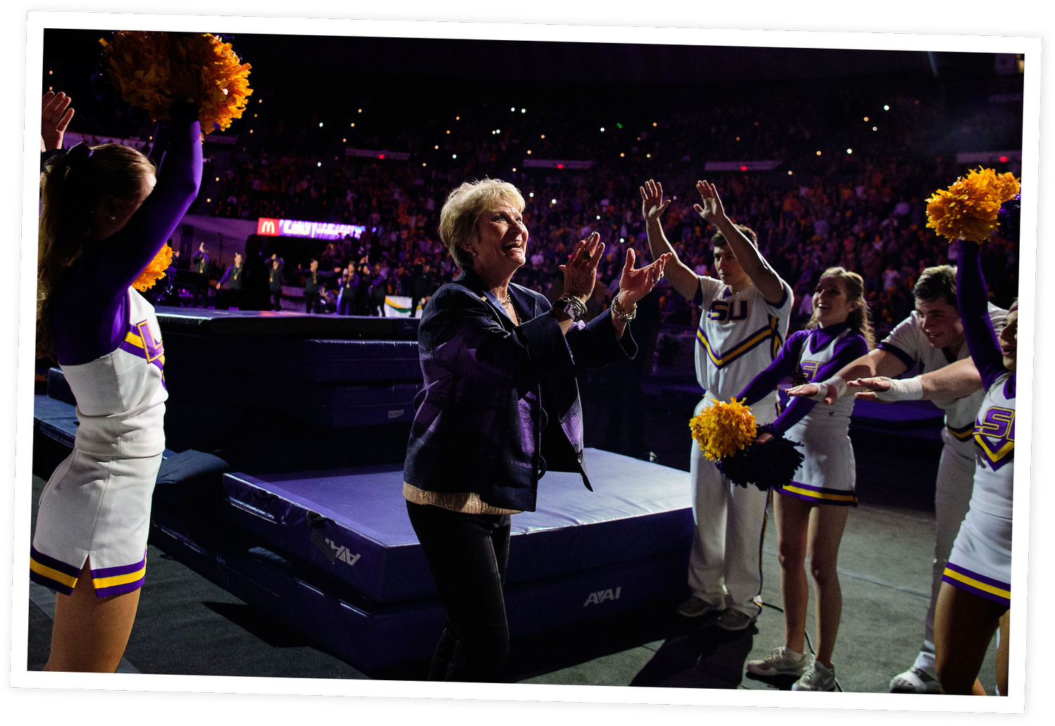 Cheerleaders performing with pom-poms and a woman, possibly a coach or team member, clapping on a sports arena court.
